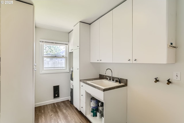 laundry room featuring baseboards, a sink, cabinet space, and wood finished floors