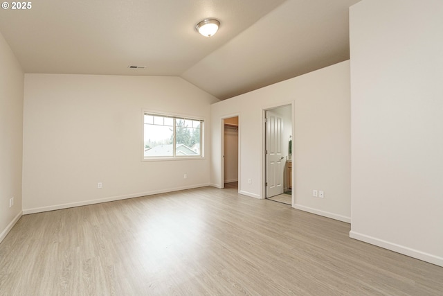 unfurnished bedroom featuring ensuite bathroom, a walk in closet, vaulted ceiling, a closet, and light hardwood / wood-style floors