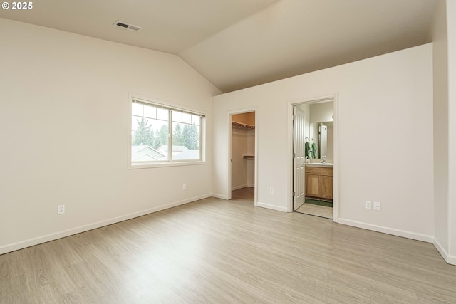 unfurnished bedroom featuring ensuite bathroom, lofted ceiling, a walk in closet, light hardwood / wood-style floors, and a closet