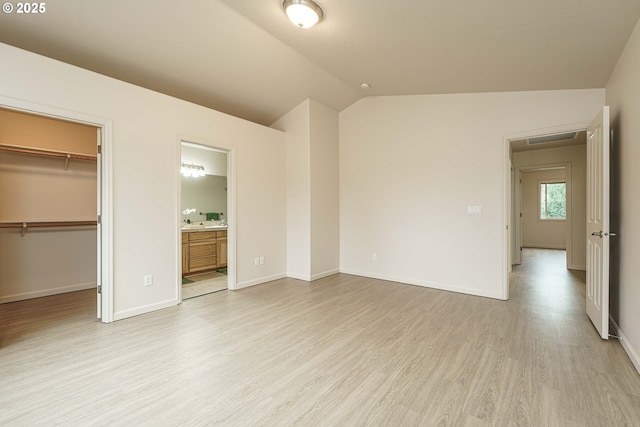 unfurnished bedroom with vaulted ceiling, ensuite bathroom, a walk in closet, light hardwood / wood-style floors, and a closet