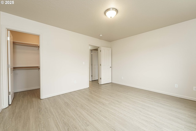 unfurnished bedroom featuring a spacious closet, a textured ceiling, light wood-type flooring, and a closet