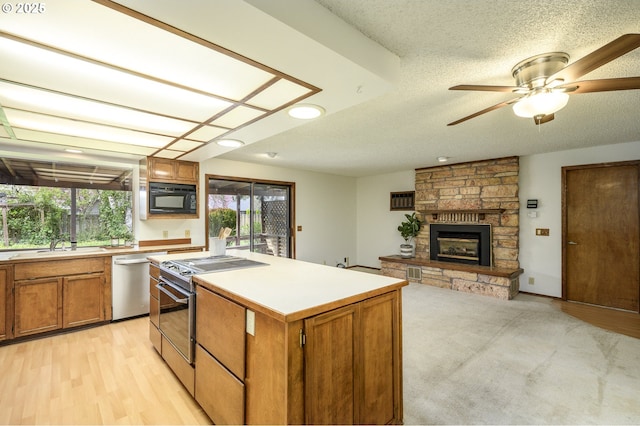 kitchen featuring brown cabinetry, a stone fireplace, a center island, appliances with stainless steel finishes, and light countertops