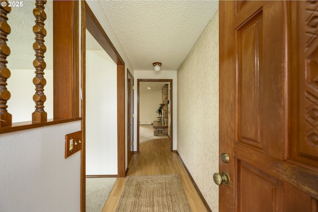 corridor with a textured ceiling, a textured wall, and light wood-style floors