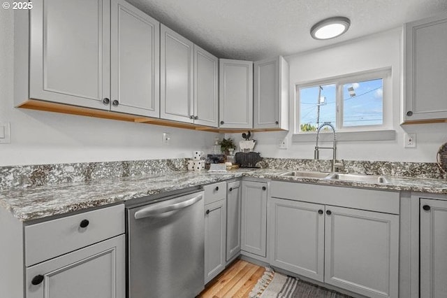 kitchen with stainless steel dishwasher, light wood-type flooring, light stone counters, a sink, and gray cabinetry