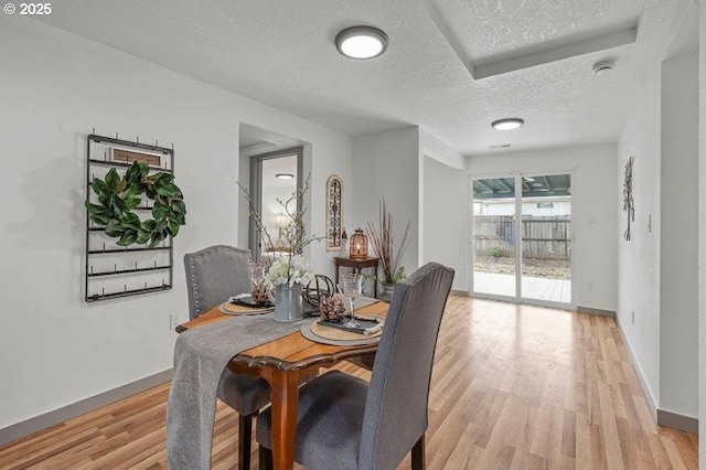 dining room with light wood-style floors, a textured ceiling, and baseboards