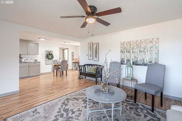 sitting room featuring baseboards, a ceiling fan, and light wood finished floors