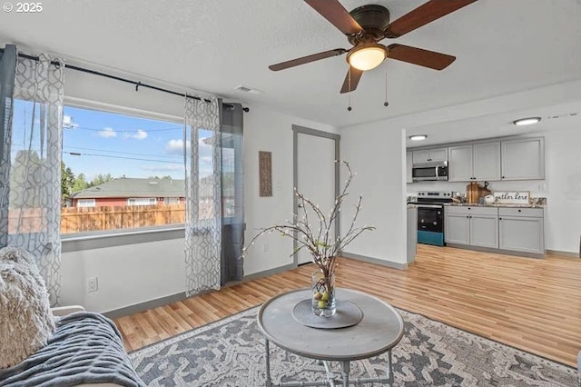 living room featuring light wood-type flooring, a ceiling fan, baseboards, and plenty of natural light