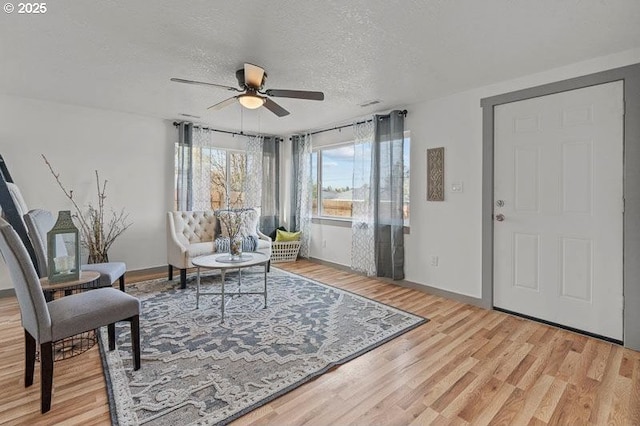living area with baseboards, a ceiling fan, a textured ceiling, and wood finished floors