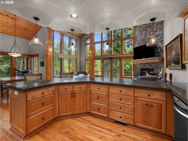 kitchen featuring a stone fireplace, dishwashing machine, tile counters, light wood-style flooring, and vaulted ceiling