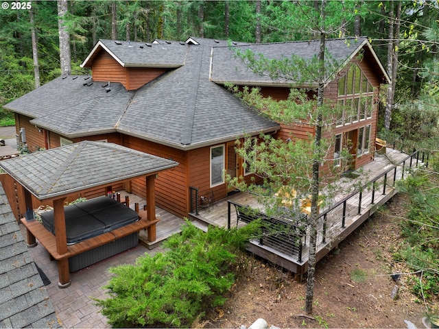back of house with a shingled roof, a deck, and a forest view
