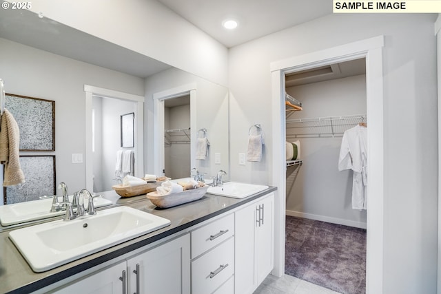 full bath with double vanity, baseboards, a walk in closet, and recessed lighting
