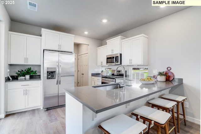 kitchen with appliances with stainless steel finishes, light wood-type flooring, a kitchen bar, white cabinetry, and recessed lighting