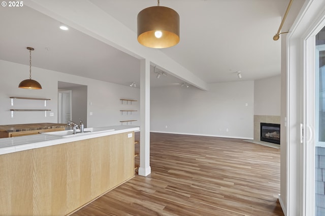 kitchen with a tile fireplace, hardwood / wood-style floors, sink, hanging light fixtures, and beam ceiling