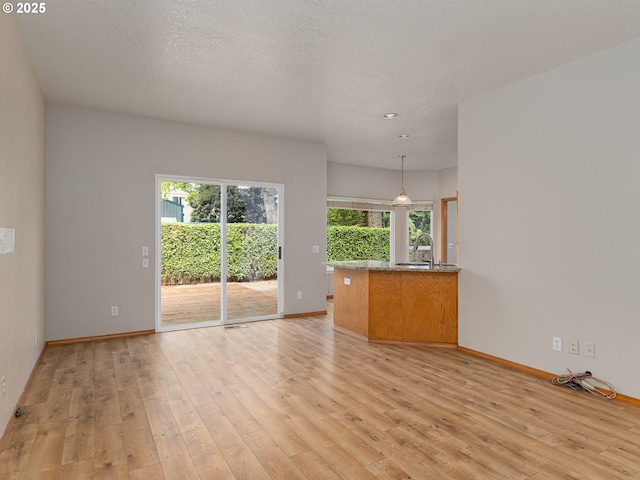 unfurnished living room featuring light wood-type flooring, a sink, and baseboards