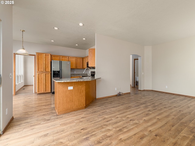 kitchen with brown cabinets, stainless steel refrigerator with ice dispenser, arched walkways, and light wood-style flooring