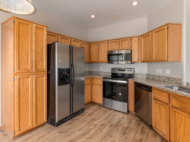 kitchen with light stone countertops, light wood-type flooring, recessed lighting, a sink, and appliances with stainless steel finishes