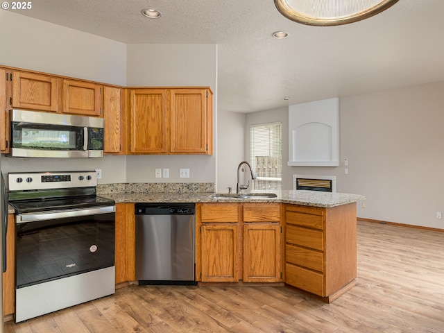 kitchen featuring a peninsula, light stone countertops, light wood-type flooring, a sink, and appliances with stainless steel finishes