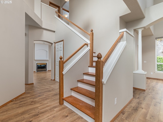 stairway with ornate columns, a glass covered fireplace, wood finished floors, and a towering ceiling