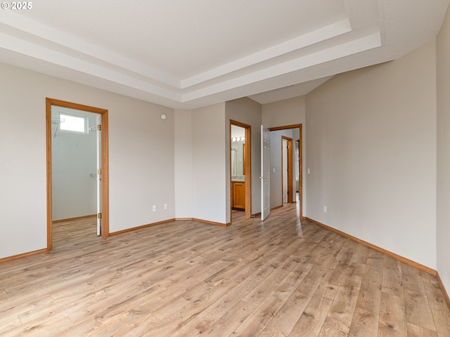 spare room with baseboards, light wood finished floors, and a raised ceiling
