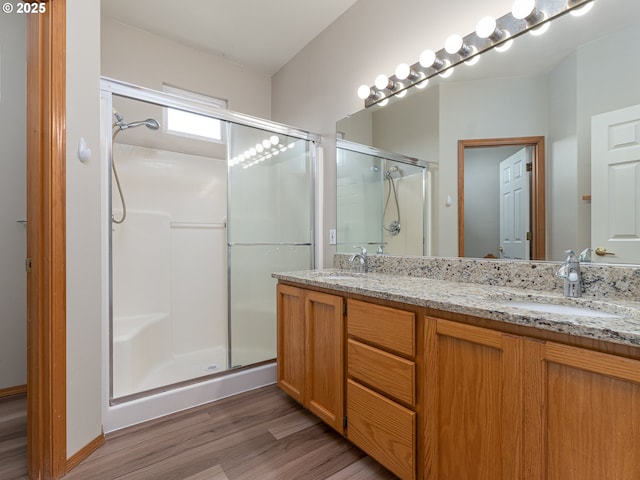full bathroom with a sink, double vanity, a shower stall, and wood finished floors