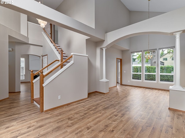 unfurnished living room featuring arched walkways, high vaulted ceiling, baseboards, a chandelier, and light wood-style flooring