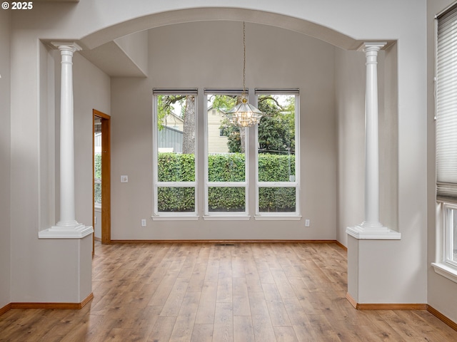 unfurnished dining area featuring ornate columns, baseboards, and light wood finished floors