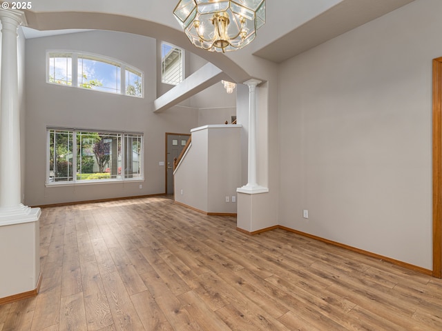 unfurnished living room featuring a healthy amount of sunlight, ornate columns, and light wood-style flooring