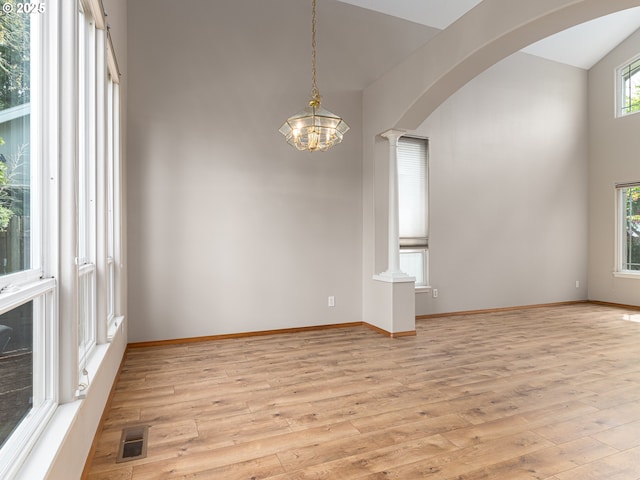 unfurnished room featuring baseboards, arched walkways, light wood finished floors, and a chandelier