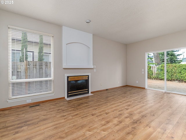 unfurnished living room featuring visible vents, a fireplace with flush hearth, light wood-style flooring, and baseboards
