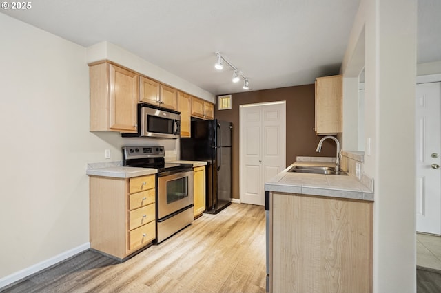 kitchen with stainless steel appliances, sink, light brown cabinetry, and light hardwood / wood-style flooring