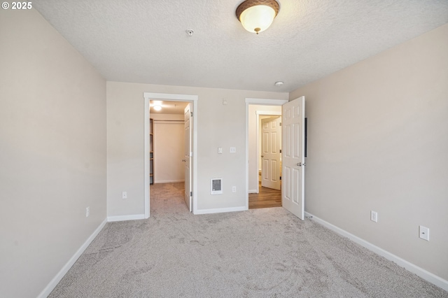 unfurnished bedroom featuring a walk in closet, a textured ceiling, a closet, and light carpet