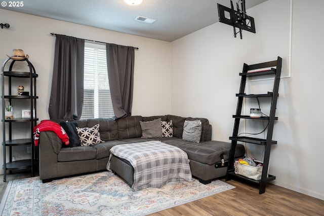 living room featuring visible vents, a textured ceiling, baseboards, and wood finished floors