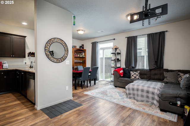 living area with visible vents, a textured ceiling, baseboards, and wood finished floors