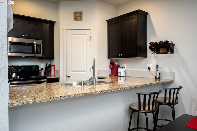 kitchen with stainless steel microwave, a kitchen bar, light stone counters, electric range, and a sink