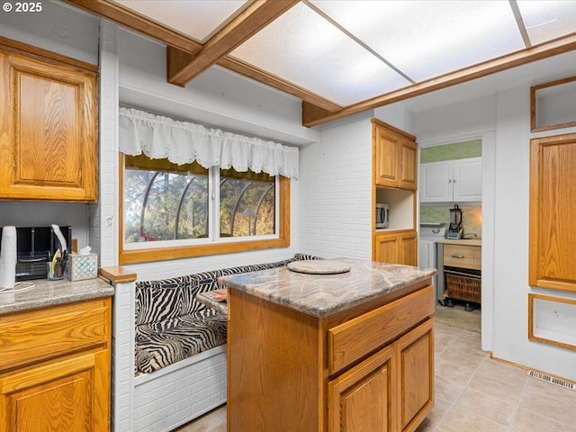 kitchen featuring light stone counters, beam ceiling, light tile patterned flooring, and a kitchen island