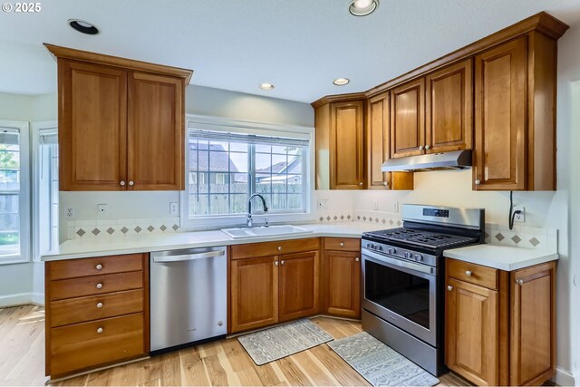 kitchen featuring stainless steel appliances, a sink, under cabinet range hood, light wood-type flooring, and brown cabinetry
