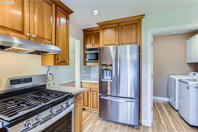 kitchen featuring stainless steel appliances, under cabinet range hood, washer and clothes dryer, light wood-style floors, and recessed lighting