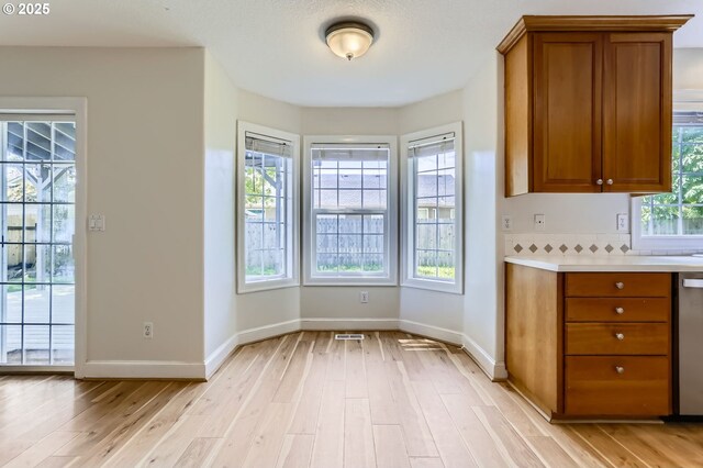 kitchen with brown cabinetry, light wood-type flooring, light countertops, baseboards, and stainless steel dishwasher