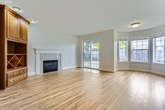 unfurnished living room featuring light wood-type flooring, a tiled fireplace, and baseboards
