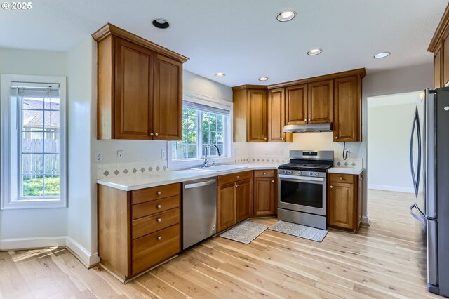 kitchen featuring stainless steel appliances, under cabinet range hood, a sink, light wood-type flooring, and brown cabinets