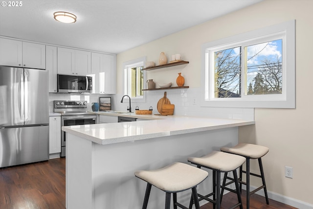 kitchen with appliances with stainless steel finishes, a kitchen bar, white cabinetry, sink, and kitchen peninsula