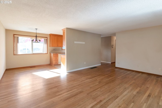 2110 SE 148th Pl, Portland, OR 97233 - unfurnished living room featuring a textured ceiling, baseboards, visible vents, light wood-style floors, and a notable chandelier