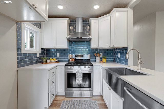 kitchen featuring stainless steel appliances, wall chimney exhaust hood, a sink, light countertops, and decorative backsplash