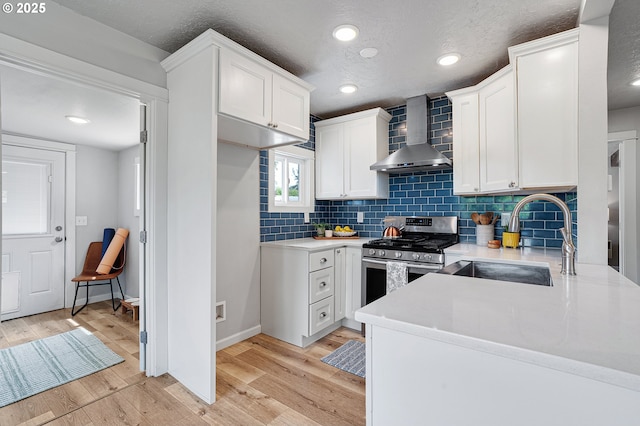 kitchen with wall chimney range hood, stainless steel range with gas stovetop, a sink, decorative backsplash, and light countertops