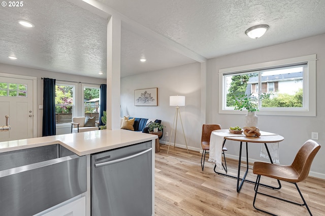 kitchen with stainless steel dishwasher, a textured ceiling, light wood-style flooring, a sink, and light countertops