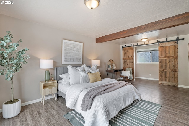 bedroom featuring wood finished floors, baseboards, a barn door, beam ceiling, and a textured ceiling