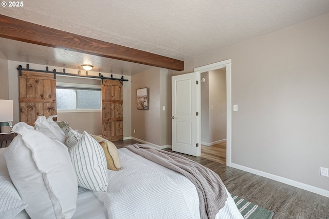 bedroom with wood finished floors, a barn door, baseboards, a textured ceiling, and beamed ceiling
