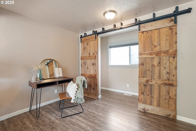 home office with a barn door, wood finished floors, a textured ceiling, and baseboards