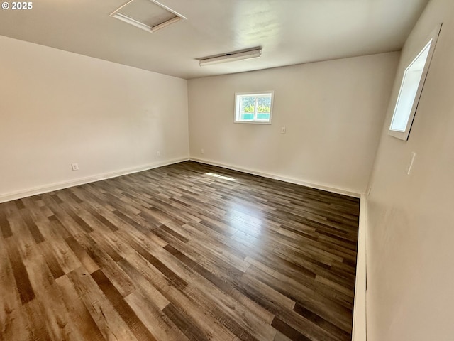 empty room with wood finished floors, attic access, and baseboards
