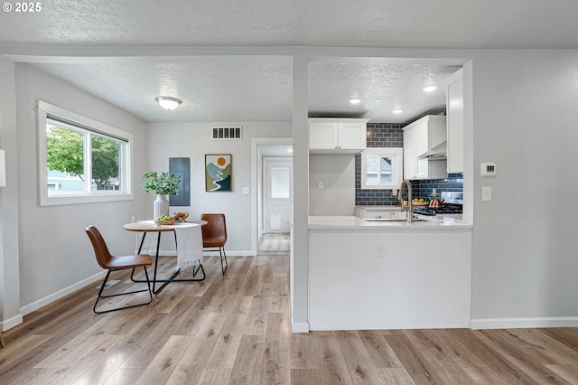 kitchen featuring light wood-type flooring, a textured ceiling, baseboards, light countertops, and tasteful backsplash